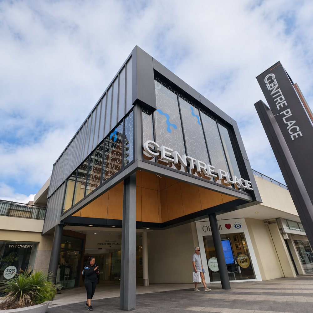 CENTRE PLACE<br>501 Victoria Street, Hamilton Central Exterior view of Centre Place shopping centre with a glass-fronted upper level and a tall sign against a blue sky with clouds.